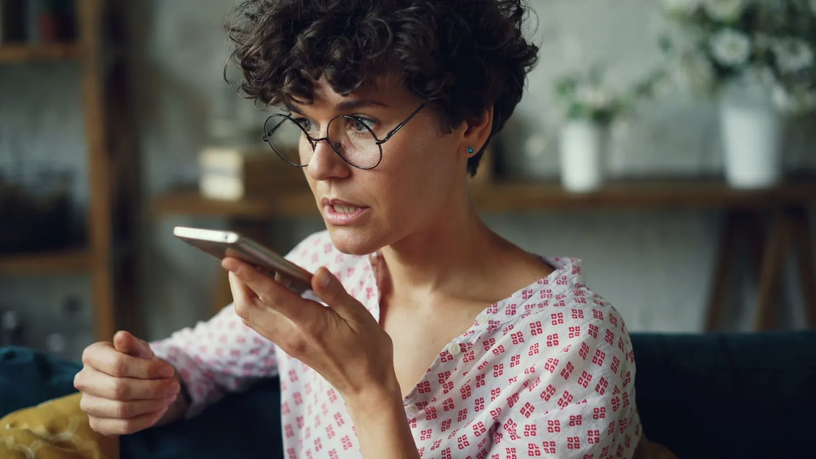Une femme dicte un message à son téléphone, assise chez elle